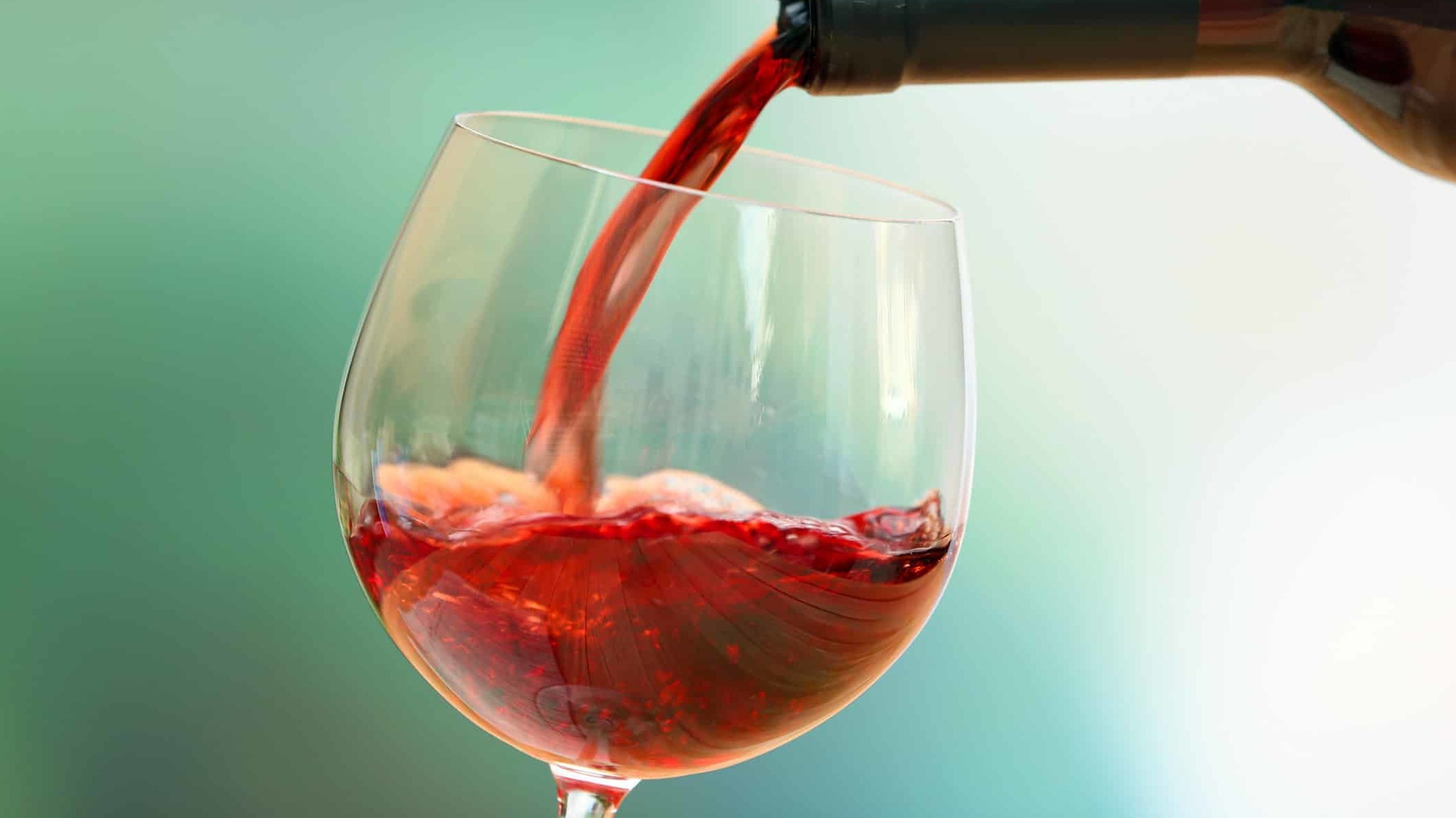 A vibrant dog park bathed in sunlight features abundant greenery with mature trees, offering ample shade for leisurely outdoor activities. In the distance is a well-equipped playground that presents an additional activity area. An inviting picnic table spreads out nearby, ideal for enjoying meals al fresco or taking relaxing breaks from play. A neatly-placed trash bin aids in maintaining the park's cleanliness for everyone's enjoyment. Dominating the scene is a generously wide dirt path gracefully curving through the expanse of grass, promising exploratory walks and lively fetch games.