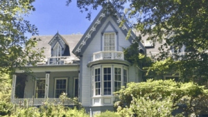 A vibrant dog park bathed in sunlight features abundant greenery with mature trees, offering ample shade for leisurely outdoor activities. In the distance is a well-equipped playground that presents an additional activity area. An inviting picnic table spreads out nearby, ideal for enjoying meals al fresco or taking relaxing breaks from play. A neatly-placed trash bin aids in maintaining the park's cleanliness for everyone's enjoyment. Dominating the scene is a generously wide dirt path gracefully curving through the expanse of grass, promising exploratory walks and lively fetch games.