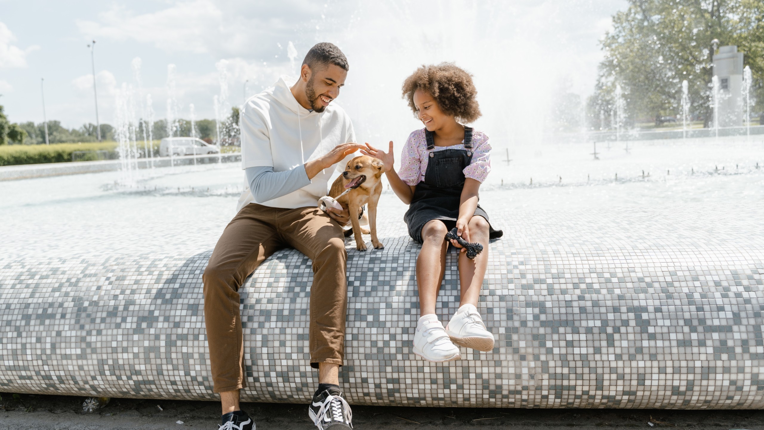 man and girl sit on ledge of fountain with dog