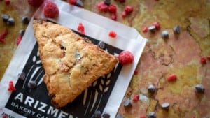 A vibrant dog park bathed in sunlight features abundant greenery with mature trees, offering ample shade for leisurely outdoor activities. In the distance is a well-equipped playground that presents an additional activity area. An inviting picnic table spreads out nearby, ideal for enjoying meals al fresco or taking relaxing breaks from play. A neatly-placed trash bin aids in maintaining the park's cleanliness for everyone's enjoyment. Dominating the scene is a generously wide dirt path gracefully curving through the expanse of grass, promising exploratory walks and lively fetch games.