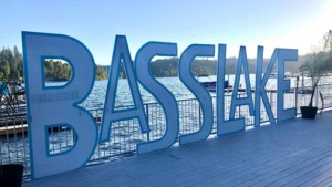 A vibrant dog park bathed in sunlight features abundant greenery with mature trees, offering ample shade for leisurely outdoor activities. In the distance is a well-equipped playground that presents an additional activity area. An inviting picnic table spreads out nearby, ideal for enjoying meals al fresco or taking relaxing breaks from play. A neatly-placed trash bin aids in maintaining the park's cleanliness for everyone's enjoyment. Dominating the scene is a generously wide dirt path gracefully curving through the expanse of grass, promising exploratory walks and lively fetch games.