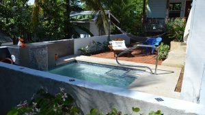 A vibrant dog park bathed in sunlight features abundant greenery with mature trees, offering ample shade for leisurely outdoor activities. In the distance is a well-equipped playground that presents an additional activity area. An inviting picnic table spreads out nearby, ideal for enjoying meals al fresco or taking relaxing breaks from play. A neatly-placed trash bin aids in maintaining the park's cleanliness for everyone's enjoyment. Dominating the scene is a generously wide dirt path gracefully curving through the expanse of grass, promising exploratory walks and lively fetch games.