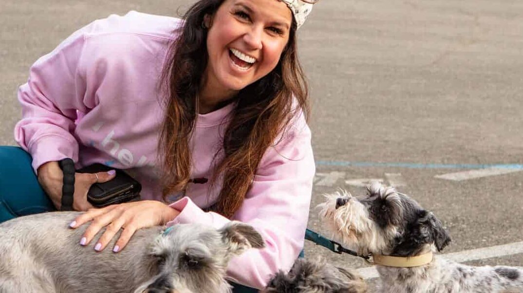 a woman kneeling down next to two dogs.