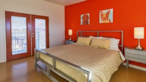 A vibrant dog park bathed in sunlight features abundant greenery with mature trees, offering ample shade for leisurely outdoor activities. In the distance is a well-equipped playground that presents an additional activity area. An inviting picnic table spreads out nearby, ideal for enjoying meals al fresco or taking relaxing breaks from play. A neatly-placed trash bin aids in maintaining the park's cleanliness for everyone's enjoyment. Dominating the scene is a generously wide dirt path gracefully curving through the expanse of grass, promising exploratory walks and lively fetch games.