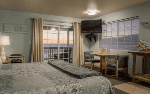 A vibrant dog park bathed in sunlight features abundant greenery with mature trees, offering ample shade for leisurely outdoor activities. In the distance is a well-equipped playground that presents an additional activity area. An inviting picnic table spreads out nearby, ideal for enjoying meals al fresco or taking relaxing breaks from play. A neatly-placed trash bin aids in maintaining the park's cleanliness for everyone's enjoyment. Dominating the scene is a generously wide dirt path gracefully curving through the expanse of grass, promising exploratory walks and lively fetch games.