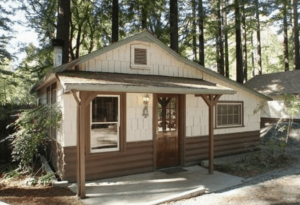 A vibrant dog park bathed in sunlight features abundant greenery with mature trees, offering ample shade for leisurely outdoor activities. In the distance is a well-equipped playground that presents an additional activity area. An inviting picnic table spreads out nearby, ideal for enjoying meals al fresco or taking relaxing breaks from play. A neatly-placed trash bin aids in maintaining the park's cleanliness for everyone's enjoyment. Dominating the scene is a generously wide dirt path gracefully curving through the expanse of grass, promising exploratory walks and lively fetch games.