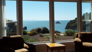 A vibrant dog park bathed in sunlight features abundant greenery with mature trees, offering ample shade for leisurely outdoor activities. In the distance is a well-equipped playground that presents an additional activity area. An inviting picnic table spreads out nearby, ideal for enjoying meals al fresco or taking relaxing breaks from play. A neatly-placed trash bin aids in maintaining the park's cleanliness for everyone's enjoyment. Dominating the scene is a generously wide dirt path gracefully curving through the expanse of grass, promising exploratory walks and lively fetch games.