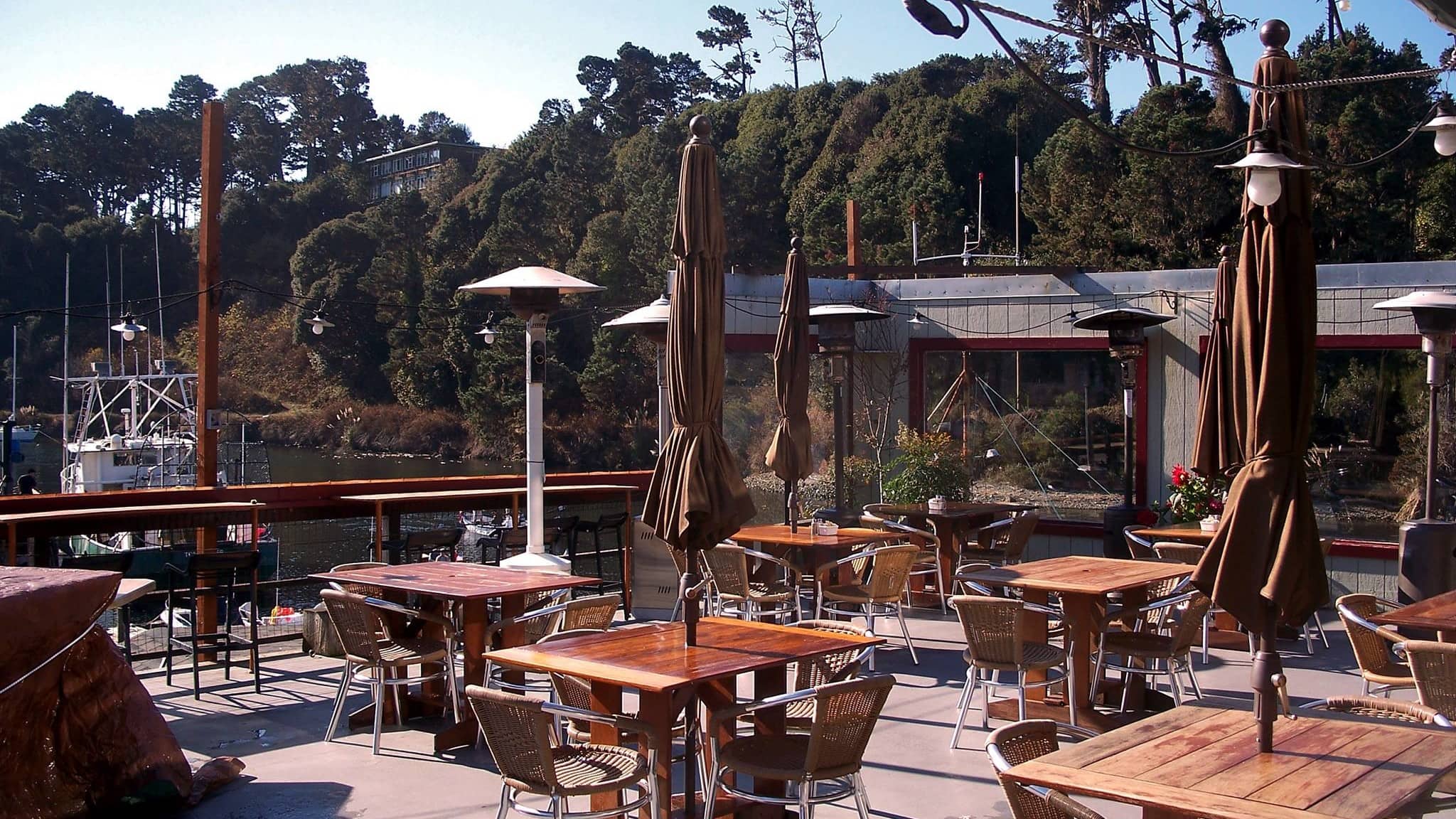 A vibrant dog park bathed in sunlight features abundant greenery with mature trees, offering ample shade for leisurely outdoor activities. In the distance is a well-equipped playground that presents an additional activity area. An inviting picnic table spreads out nearby, ideal for enjoying meals al fresco or taking relaxing breaks from play. A neatly-placed trash bin aids in maintaining the park's cleanliness for everyone's enjoyment. Dominating the scene is a generously wide dirt path gracefully curving through the expanse of grass, promising exploratory walks and lively fetch games.