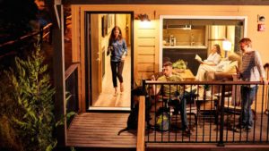 A vibrant dog park bathed in sunlight features abundant greenery with mature trees, offering ample shade for leisurely outdoor activities. In the distance is a well-equipped playground that presents an additional activity area. An inviting picnic table spreads out nearby, ideal for enjoying meals al fresco or taking relaxing breaks from play. A neatly-placed trash bin aids in maintaining the park's cleanliness for everyone's enjoyment. Dominating the scene is a generously wide dirt path gracefully curving through the expanse of grass, promising exploratory walks and lively fetch games.