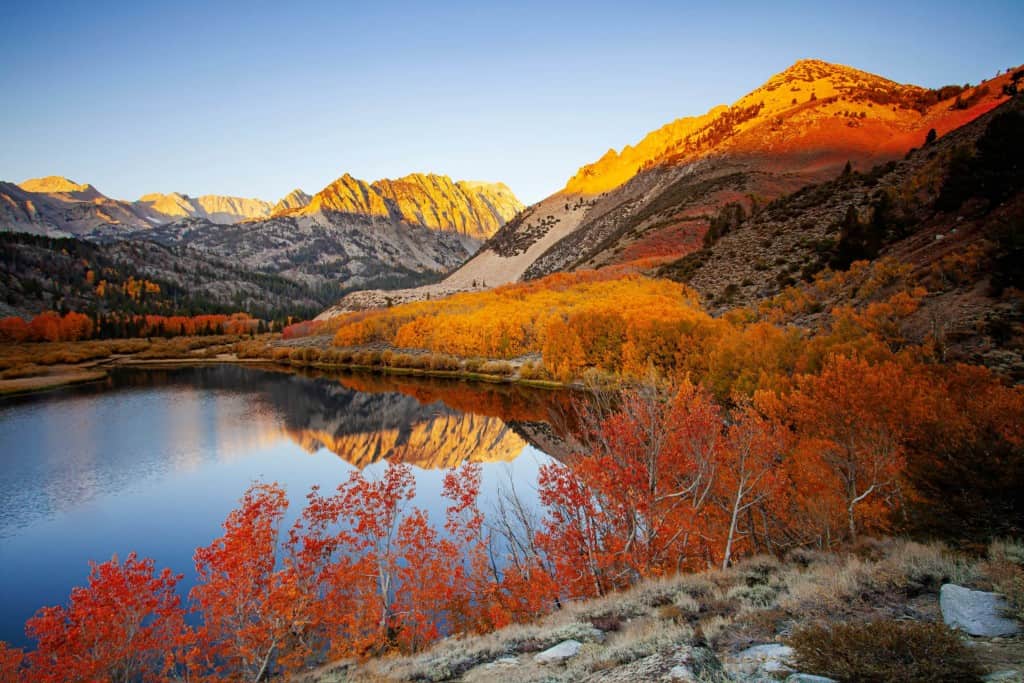 View of mountain lake surrounded by trees with vibrant red, orange and yellow leaves