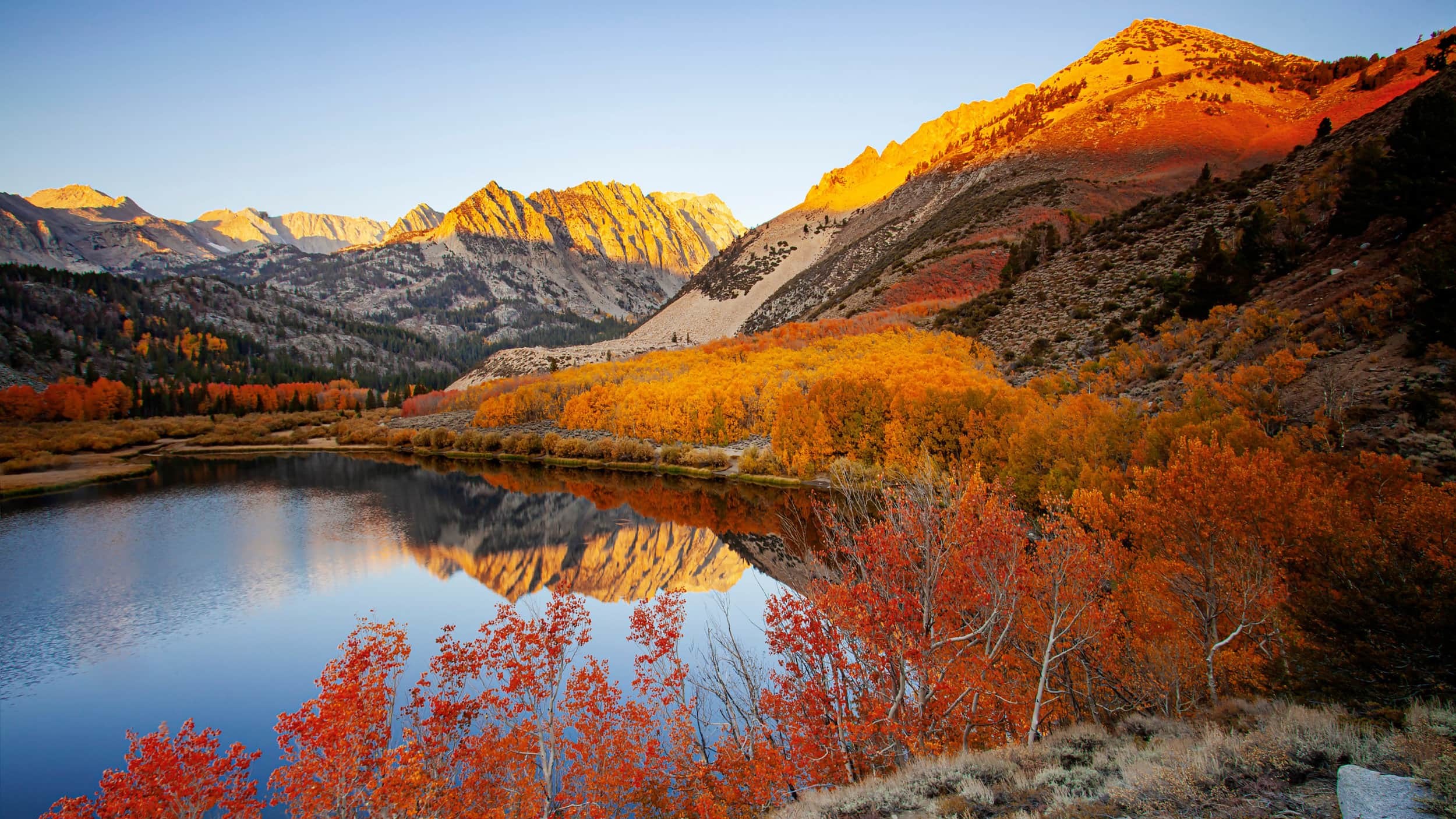 View of mountain lake surrounded by trees with vibrant red, orange and yellow leaves