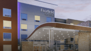 A vibrant dog park bathed in sunlight features abundant greenery with mature trees, offering ample shade for leisurely outdoor activities. In the distance is a well-equipped playground that presents an additional activity area. An inviting picnic table spreads out nearby, ideal for enjoying meals al fresco or taking relaxing breaks from play. A neatly-placed trash bin aids in maintaining the park's cleanliness for everyone's enjoyment. Dominating the scene is a generously wide dirt path gracefully curving through the expanse of grass, promising exploratory walks and lively fetch games.