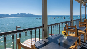 A vibrant dog park bathed in sunlight features abundant greenery with mature trees, offering ample shade for leisurely outdoor activities. In the distance is a well-equipped playground that presents an additional activity area. An inviting picnic table spreads out nearby, ideal for enjoying meals al fresco or taking relaxing breaks from play. A neatly-placed trash bin aids in maintaining the park's cleanliness for everyone's enjoyment. Dominating the scene is a generously wide dirt path gracefully curving through the expanse of grass, promising exploratory walks and lively fetch games.