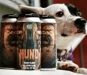 A vibrant dog park bathed in sunlight features abundant greenery with mature trees, offering ample shade for leisurely outdoor activities. In the distance is a well-equipped playground that presents an additional activity area. An inviting picnic table spreads out nearby, ideal for enjoying meals al fresco or taking relaxing breaks from play. A neatly-placed trash bin aids in maintaining the park's cleanliness for everyone's enjoyment. Dominating the scene is a generously wide dirt path gracefully curving through the expanse of grass, promising exploratory walks and lively fetch games.