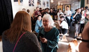 A vibrant dog park bathed in sunlight features abundant greenery with mature trees, offering ample shade for leisurely outdoor activities. In the distance is a well-equipped playground that presents an additional activity area. An inviting picnic table spreads out nearby, ideal for enjoying meals al fresco or taking relaxing breaks from play. A neatly-placed trash bin aids in maintaining the park's cleanliness for everyone's enjoyment. Dominating the scene is a generously wide dirt path gracefully curving through the expanse of grass, promising exploratory walks and lively fetch games.