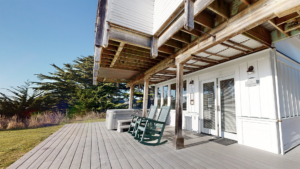 A vibrant dog park bathed in sunlight features abundant greenery with mature trees, offering ample shade for leisurely outdoor activities. In the distance is a well-equipped playground that presents an additional activity area. An inviting picnic table spreads out nearby, ideal for enjoying meals al fresco or taking relaxing breaks from play. A neatly-placed trash bin aids in maintaining the park's cleanliness for everyone's enjoyment. Dominating the scene is a generously wide dirt path gracefully curving through the expanse of grass, promising exploratory walks and lively fetch games.