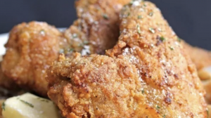 A vibrant dog park bathed in sunlight features abundant greenery with mature trees, offering ample shade for leisurely outdoor activities. In the distance is a well-equipped playground that presents an additional activity area. An inviting picnic table spreads out nearby, ideal for enjoying meals al fresco or taking relaxing breaks from play. A neatly-placed trash bin aids in maintaining the park's cleanliness for everyone's enjoyment. Dominating the scene is a generously wide dirt path gracefully curving through the expanse of grass, promising exploratory walks and lively fetch games.