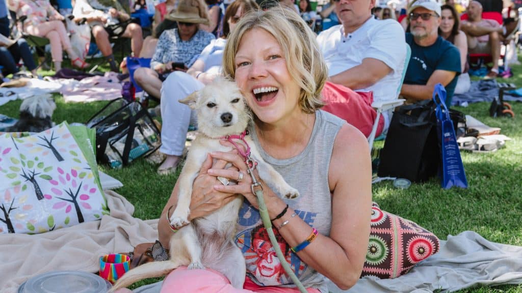 A woman holding a small dog at the Woofstock outdoor concert. - Dogtrekker