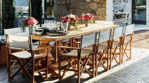 A vibrant dog park bathed in sunlight features abundant greenery with mature trees, offering ample shade for leisurely outdoor activities. In the distance is a well-equipped playground that presents an additional activity area. An inviting picnic table spreads out nearby, ideal for enjoying meals al fresco or taking relaxing breaks from play. A neatly-placed trash bin aids in maintaining the park's cleanliness for everyone's enjoyment. Dominating the scene is a generously wide dirt path gracefully curving through the expanse of grass, promising exploratory walks and lively fetch games.